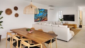 Un salon moderne avec une table à manger en bois, un canapé blanc et un grand téléviseur.
