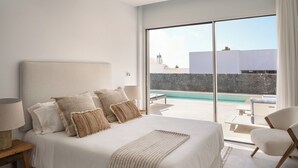 Une chambre avec un grand lit, une table de chevet, une lampe et une vue sur une piscine, visible à travers une porte-fenêtre coulissante.