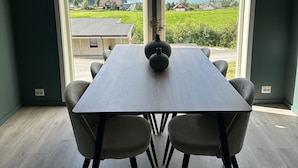Ein Essbereich mit Tisch und Stühlen, große Fenster mit Blick auf einen See und Berge sowie eine Pendelleuchte über dem Tisch.