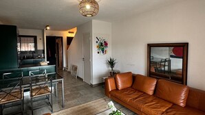 Una sala de estar moderna con un sofá de cuero marrón, una mesa de centro de mármol blanco y un comedor con una mesa y sillas verdes.