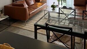 Una sala de estar moderna con un sofá de cuero marrón, una mesa de centro de vidrio y un comedor con sillas.