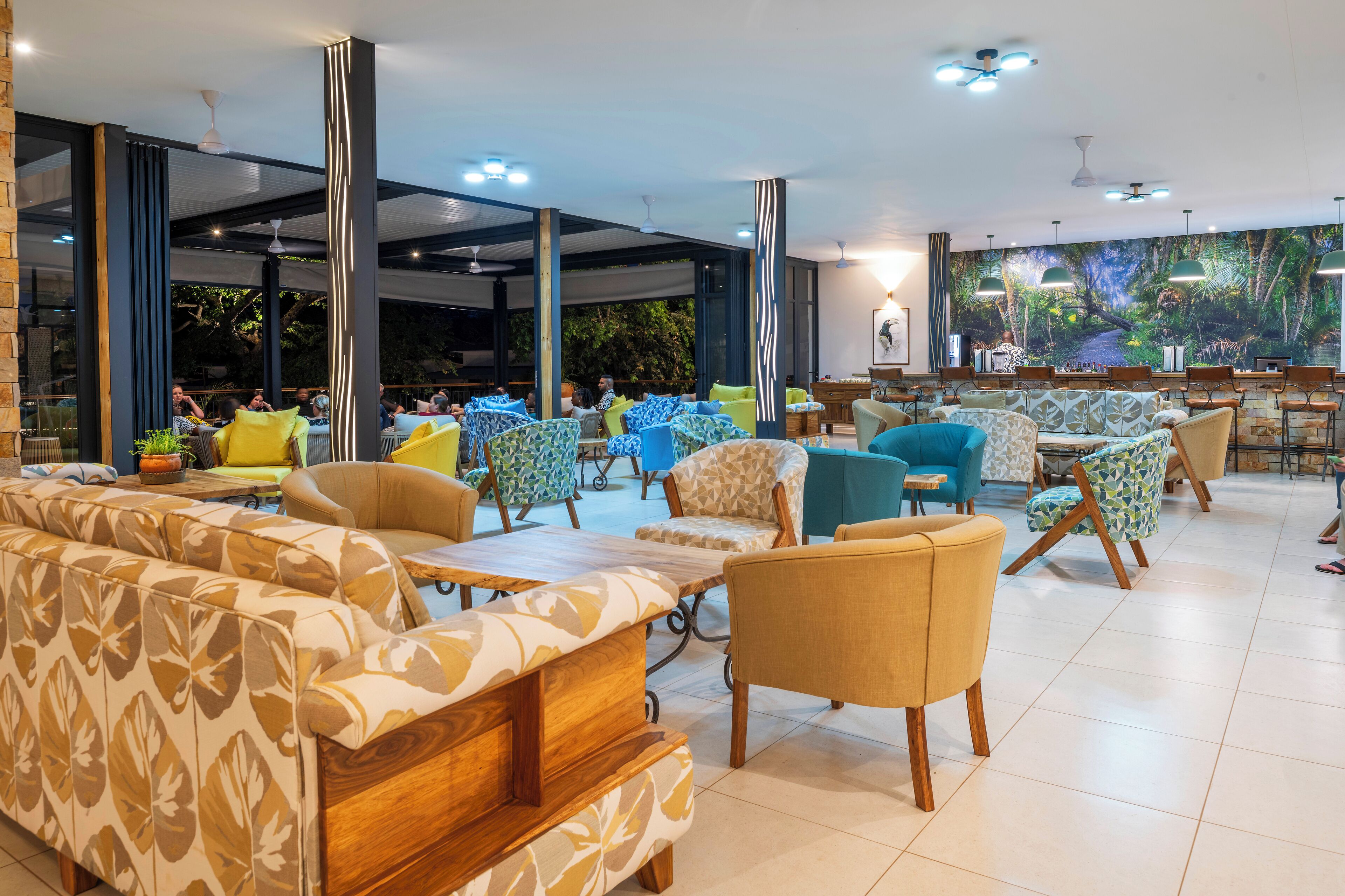 Un vaste espace intérieur aménagé avec différents types de chaises et de canapés, de grandes fenêtres et des ventilateurs de plafond.