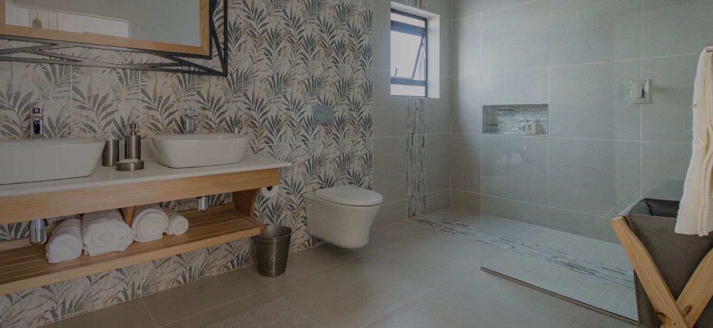 Een badkamer met een houten wastafelmeubel, twee wastafels, een toilet en een douchehoek.