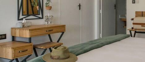 A bedroom with a bed, a desk, a chair, a mirror, and a door.