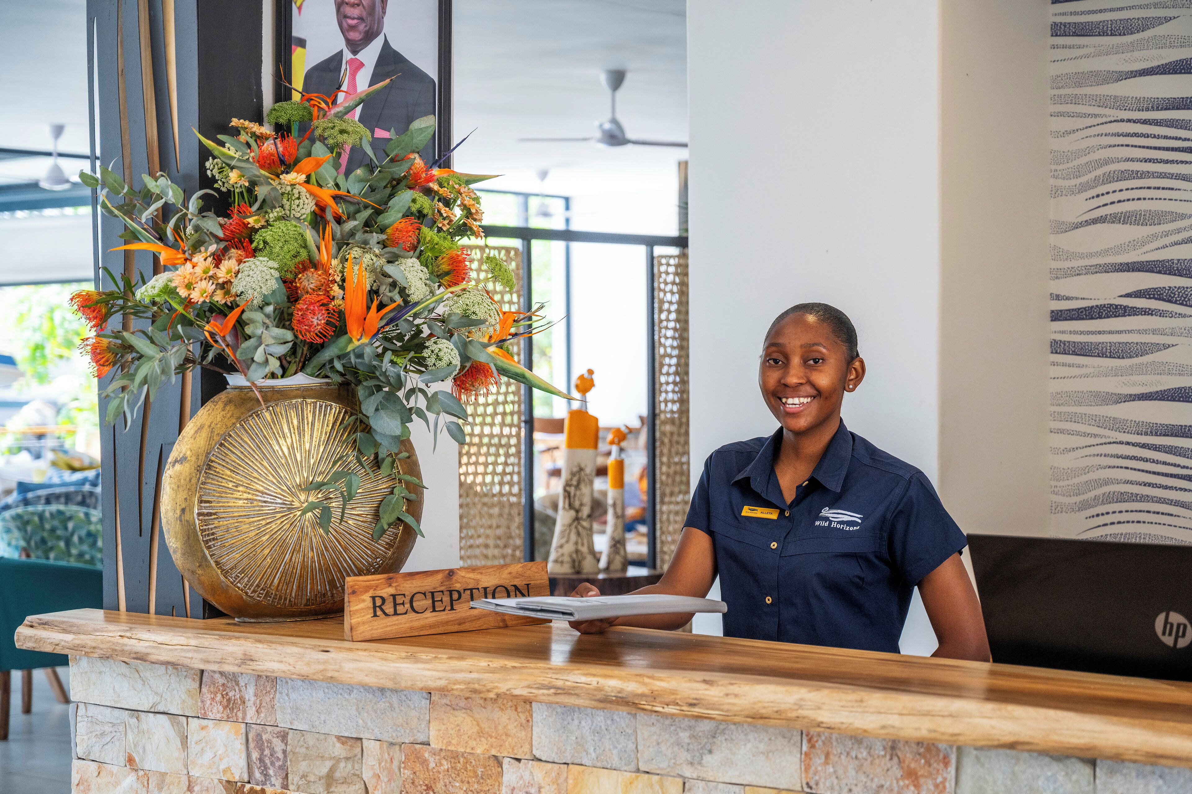 A reception desk with a wooden reception sign, a large vase of flowers, and a nameplate.