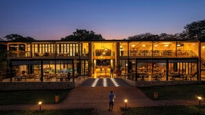 A modern building with multiple levels, large glass windows, and outdoor seating areas. - Waterfalls Lodge (Victoria Falls)