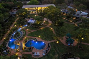 Vista aérea de un complejo turístico con varias piscinas, un edificio grande con ventanas iluminadas y jardines cuidados.