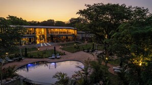 A resort with a swimming pool, outdoor seating, and a well-lit building. - Waterfalls Lodge (Victoria Falls)
