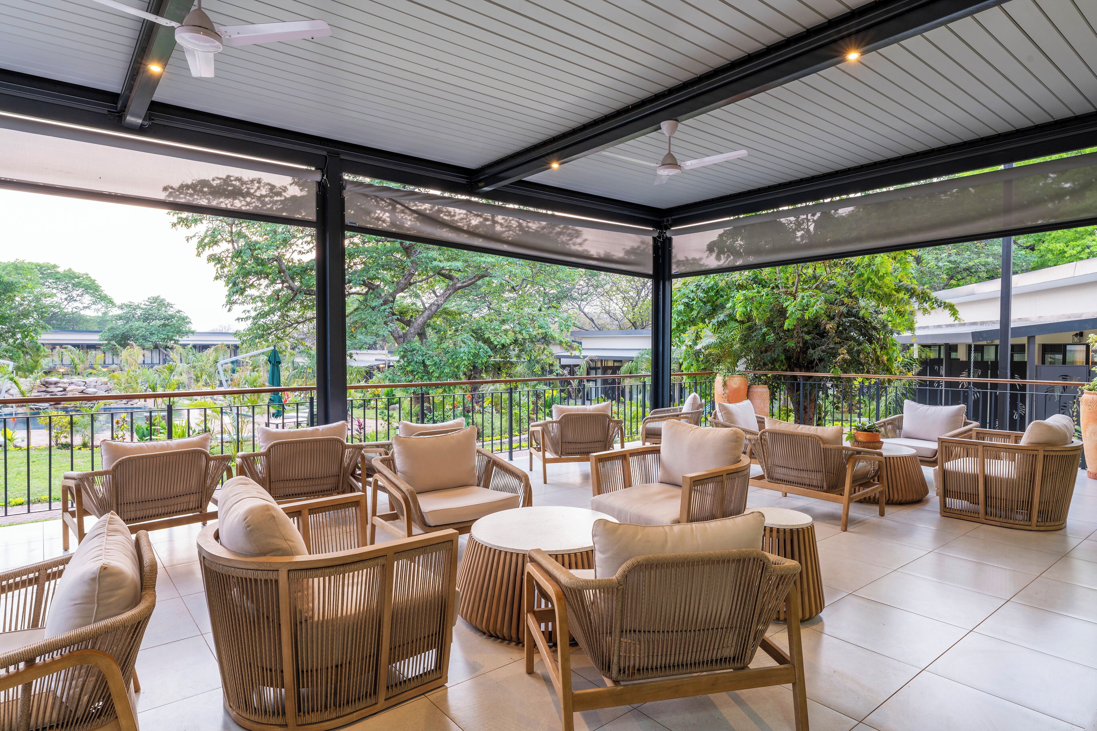 A covered outdoor seating area with wicker furniture and a view of the surrounding greenery.
