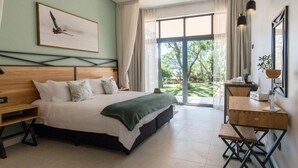 A bedroom with a large bed, a wooden desk, and a view of the outdoors. - Waterfalls Lodge (Victoria Falls)