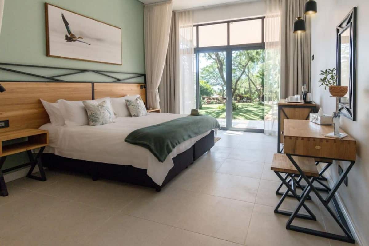 A bedroom with a large bed, a wooden desk, and a view of the outdoors.