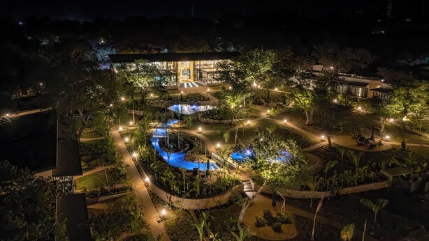 A well-lit outdoor area with a pool, pathways, and seating areas surrounded by trees. - Waterfalls Lodge (Victoria Falls)