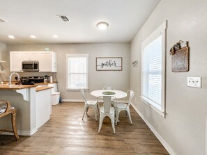 A kitchen with white cabinets, a microwave, and a dining area with a white table and chairs.