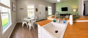 A kitchen with a sink, a dining table with chairs, a television, and a view of the outdoors. - This coastal cottage features 3 bedrooms and 2 baths, accommodating up to 6 guests (Rockport)