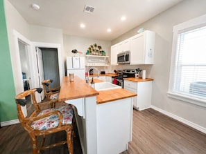 A compact kitchen with white cabinets, a wooden countertop, a built-in oven, and a microwave.
