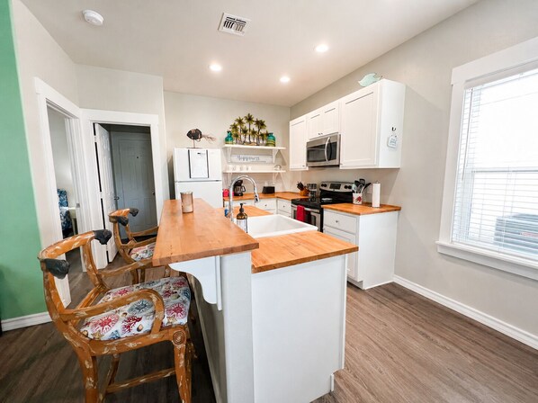 A compact kitchen with white cabinets, a wooden countertop, a built-in oven, and a microwave.