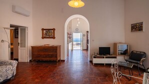 A spacious living area with a sofa, wooden cabinet, TV, and a view through an archway. - Casa sul Mare by Rentbeat (Vieste)
