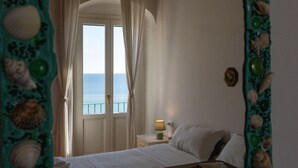 A bedroom with a bed, a nightstand, a lamp, and a view of the sea through a window. - Casa sul Mare by Rentbeat (Vieste)