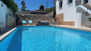 A swimming pool with a stone wall and a white building in the background.