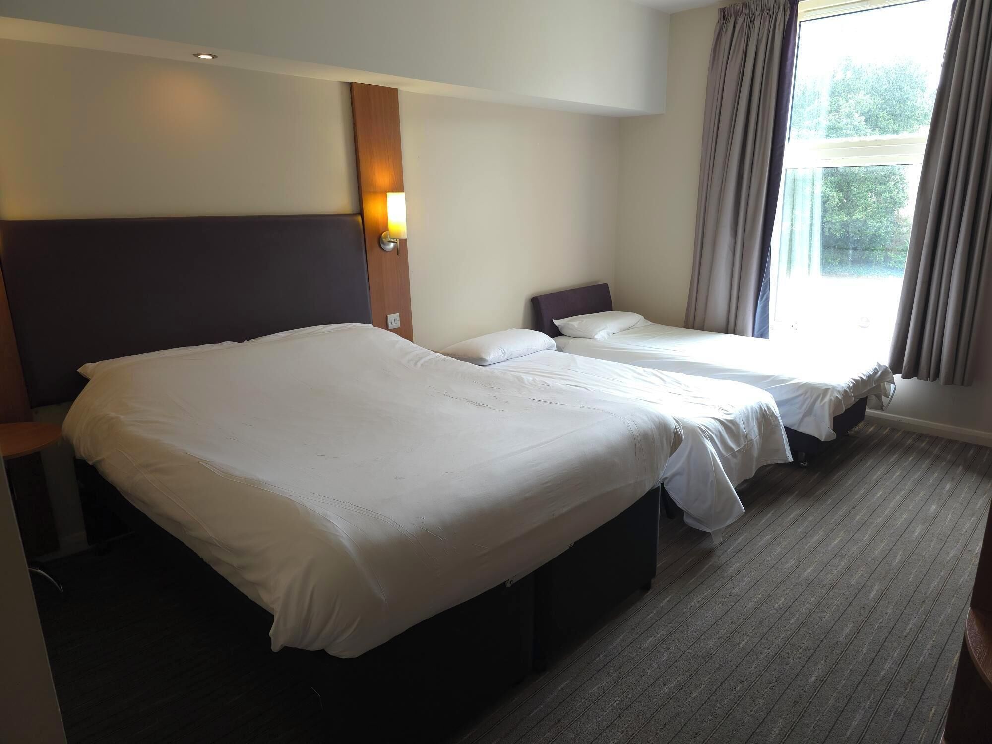A hotel room with two beds, a wooden headboard, a nightstand, and a window with curtains.