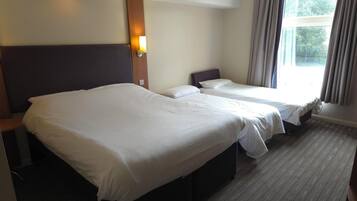 A hotel room with two beds, a wooden headboard, a nightstand, and a window with curtains.