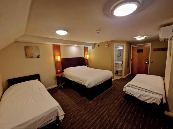 A hotel room with two beds, a small table, a wall-mounted lamp, a ceiling light, and a door leading to a bathroom. - Charter Hotel Bournemouth (Bournemouth)