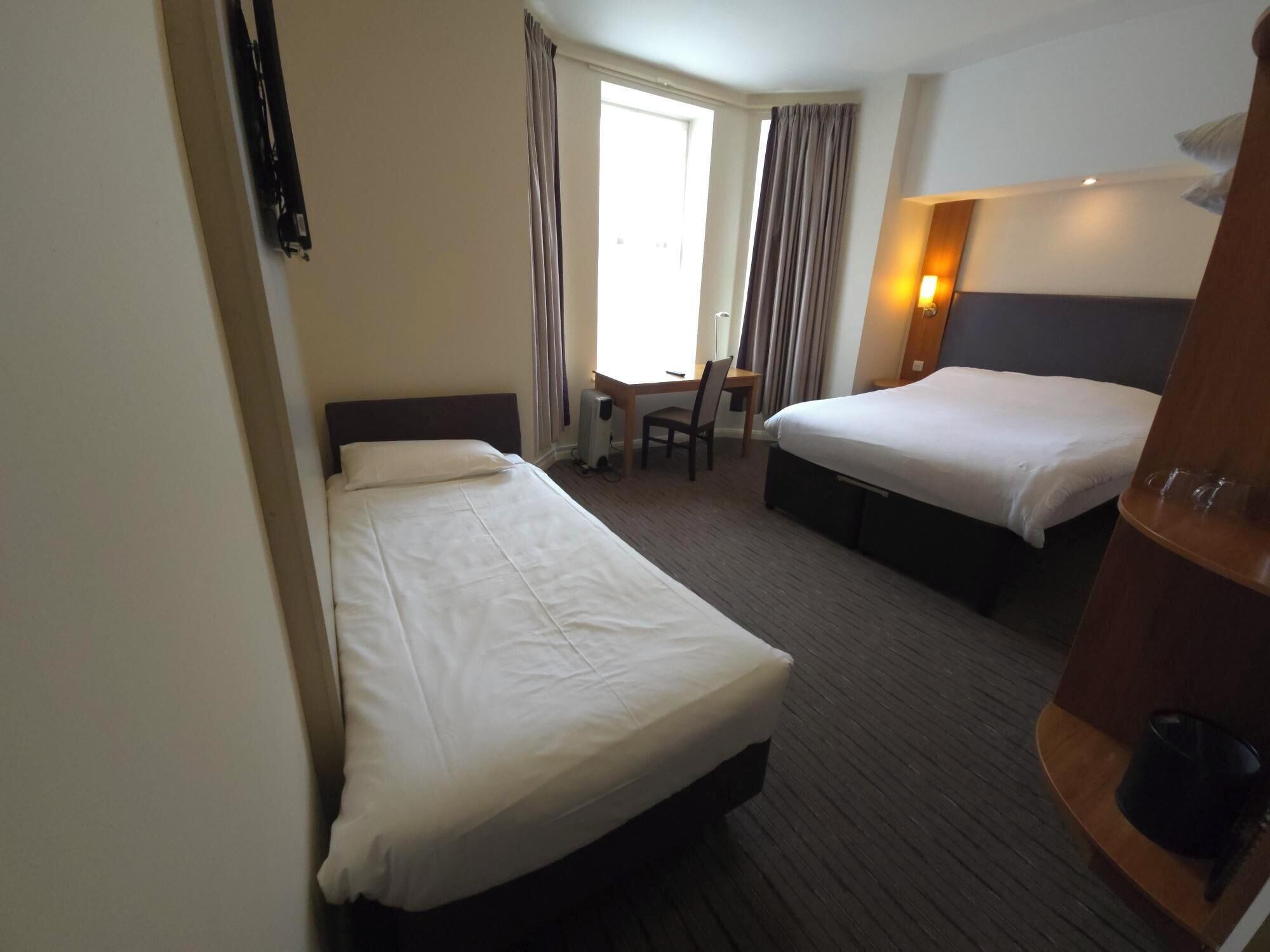 A hotel room with two single beds, a desk, a chair, and a wardrobe.