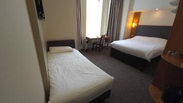 A hotel room with two single beds, a desk, a chair, and a wardrobe.