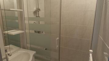 A glass-enclosed shower stall with a handheld showerhead, a glass door, and a white sink with a mirror.