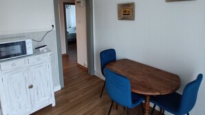Ein Essbereich mit einem Holztisch und blauen Stühlen, einem weißen Schrank mit einer Mikrowelle sowie einer hängenden Leuchte.
