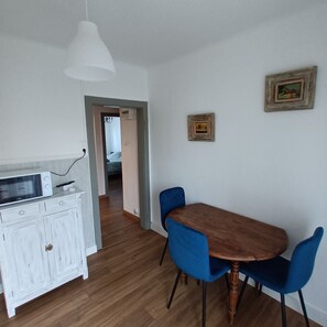 A dining area with a wooden table and blue chairs, a white cabinet with a microwave, and a hanging light fixture.