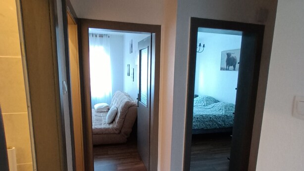 Ein schmaler Korridor mit Holzboden, der zum Schlafzimmer mit Bett und Fenster führt.