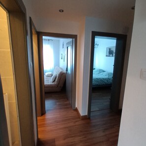 Un couloir étroit, doté d’un plancher en bois, mène à une chambre à coucher qui contient un lit et une fenêtre.