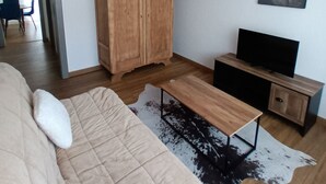 Ein modernes Wohnzimmer mit einem Holzschrank, einem Flachbildfernseher, einer Couch mit einem weißen Kissen und einem Kuhfellteppich.