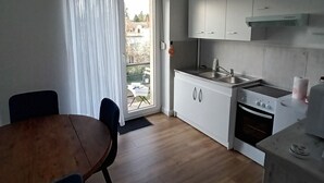 Eine kleine Küche mit weißen Schränken, einem Holztisch und Blick aus dem Fenster.