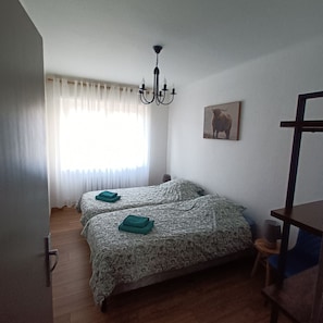 A bedroom with two beds, a chandelier, a painting of a bull, and a wooden desk.