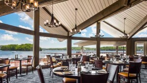 A restaurant with tables and chairs, large windows, and a view of a lake.