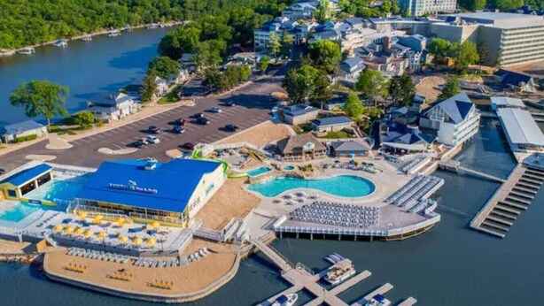 An aerial view of a waterfront property with a swimming pool, docked boats, and a variety of buildings.