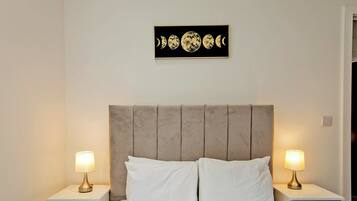 Un dormitorio con una cama, dos mesitas de noche, un cabecero y una obra de arte en la pared que representa las fases lunares.