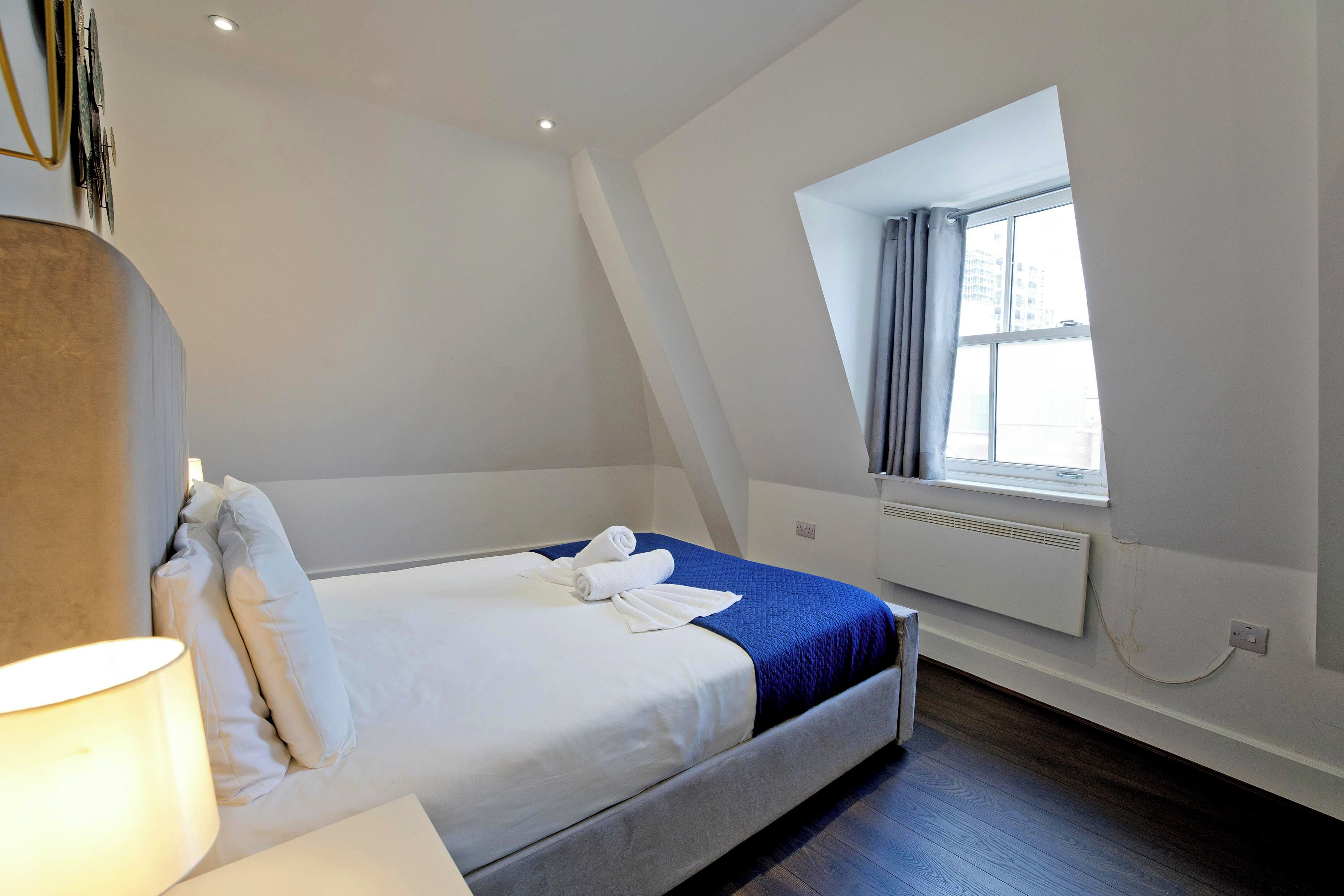 Une chambre à coucher avec un lit, une fenêtre, un radiateur et une lampe.