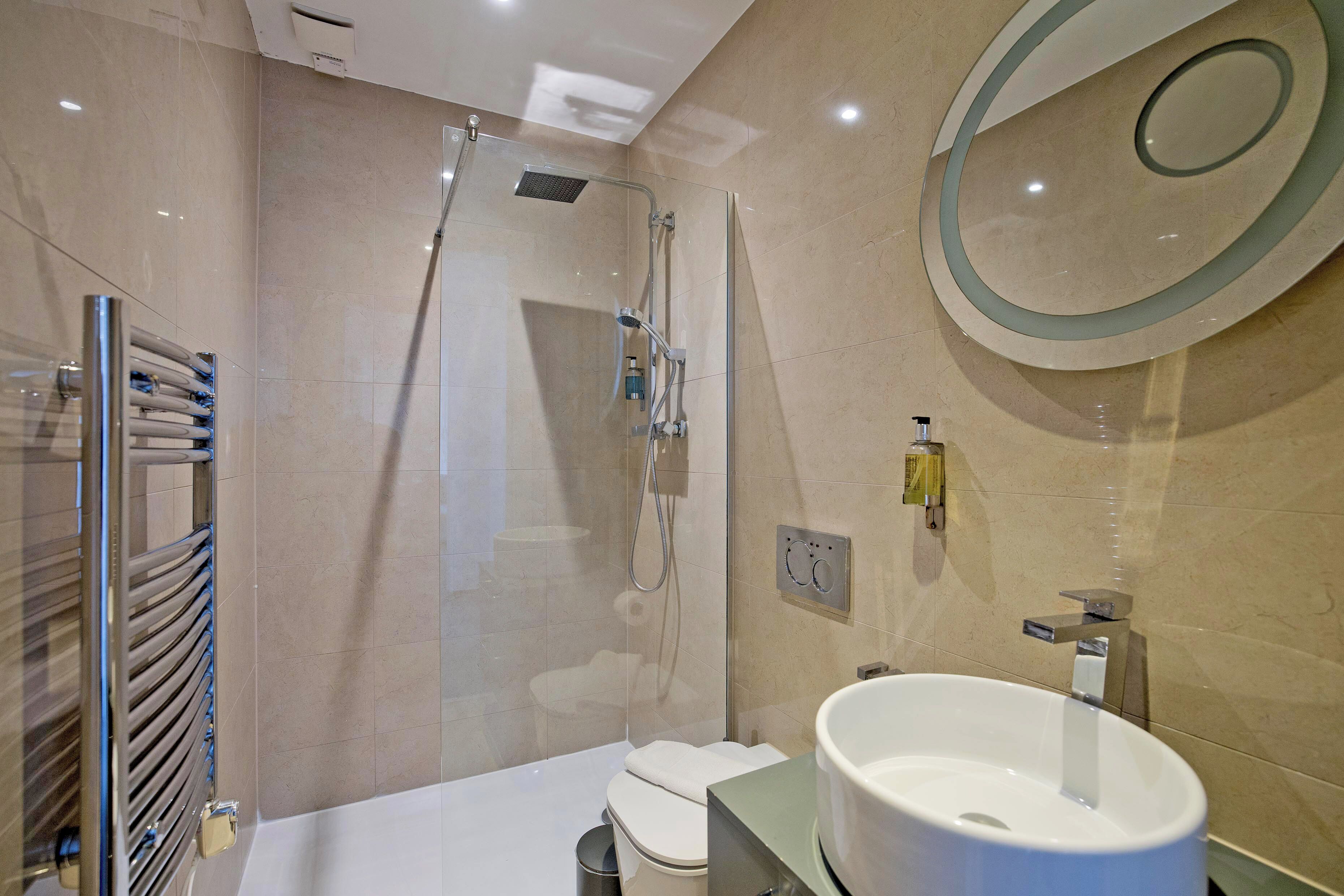 Un baño moderno con ducha envuelta en vidrio, un lavamanos blanco y un inodoro.