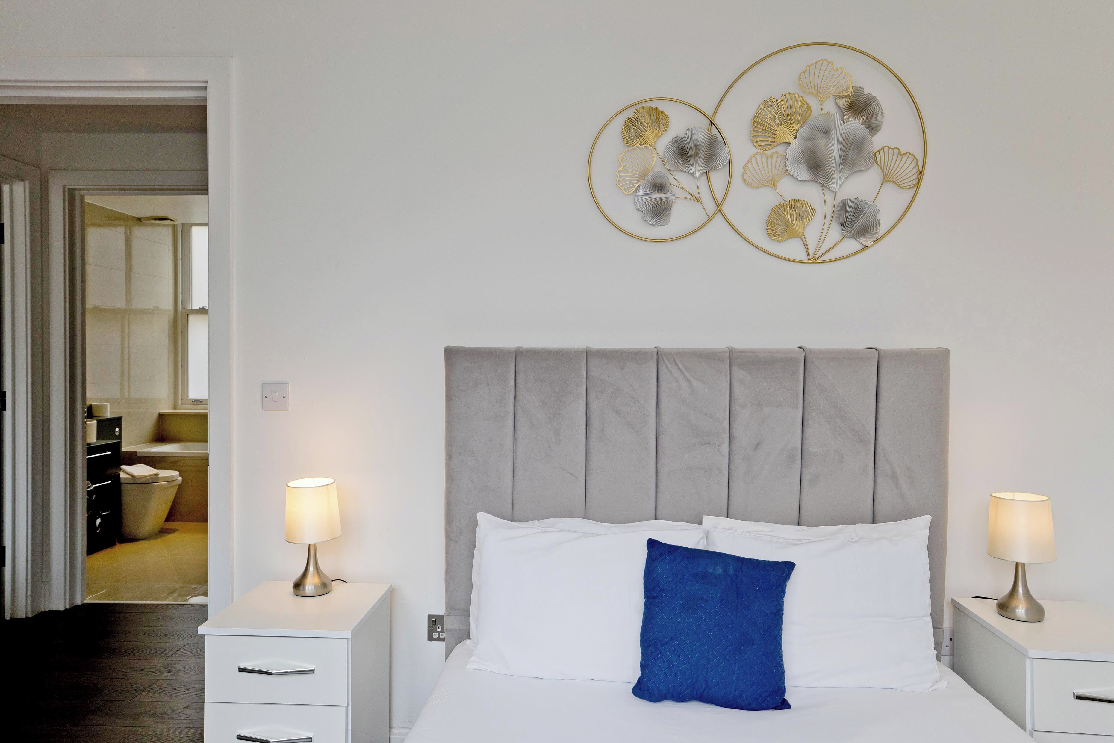 A neatly made bed with white and blue pillows, a grey headboard, and two bedside lamps on white nightstands.