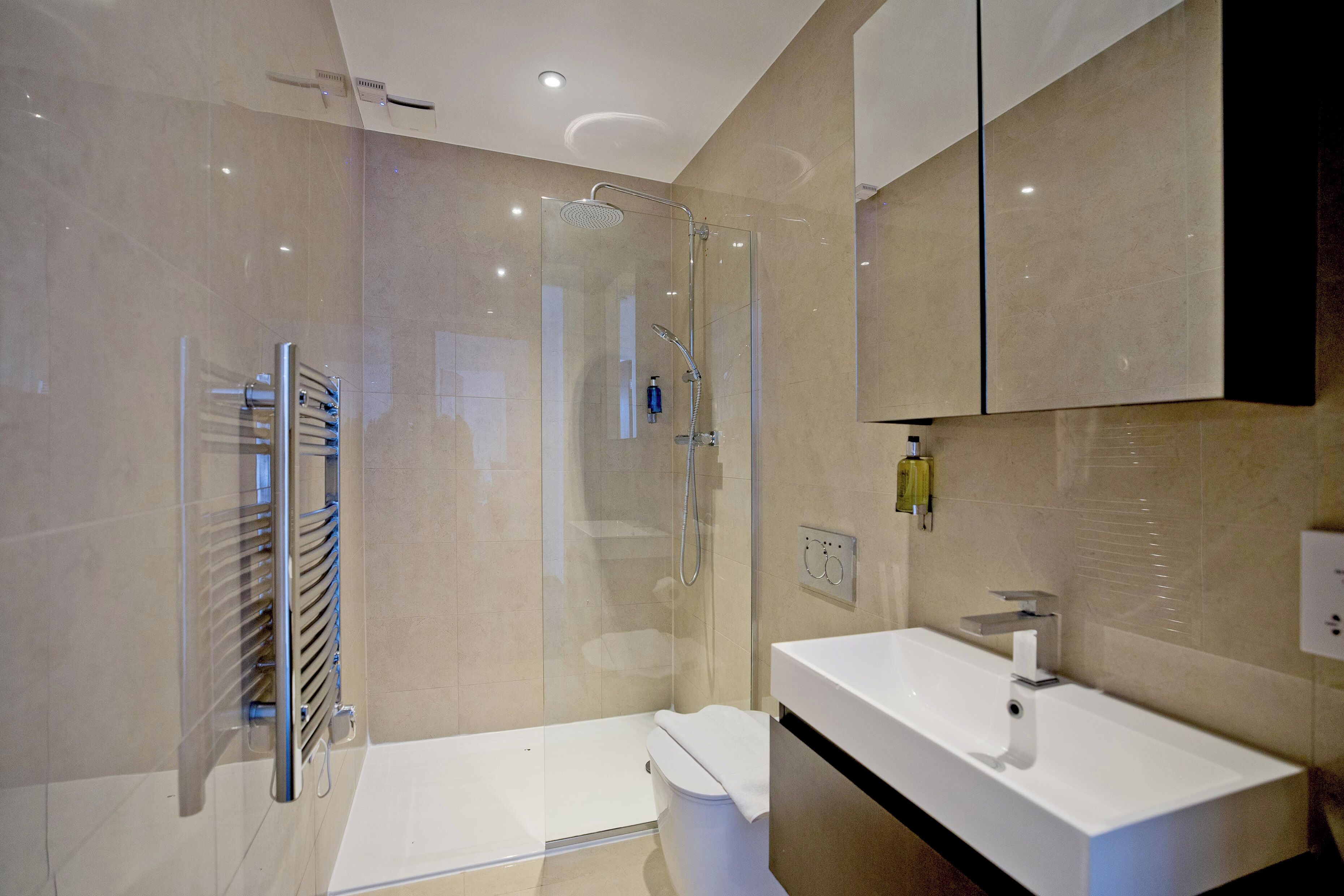 Une salle de bain moderne avec une douche à l’italienne en verre, un lavabo blanc et un grand miroir.