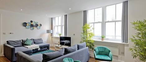 A modern living room with a grey sofa set, a teal armchair, and a small white table.