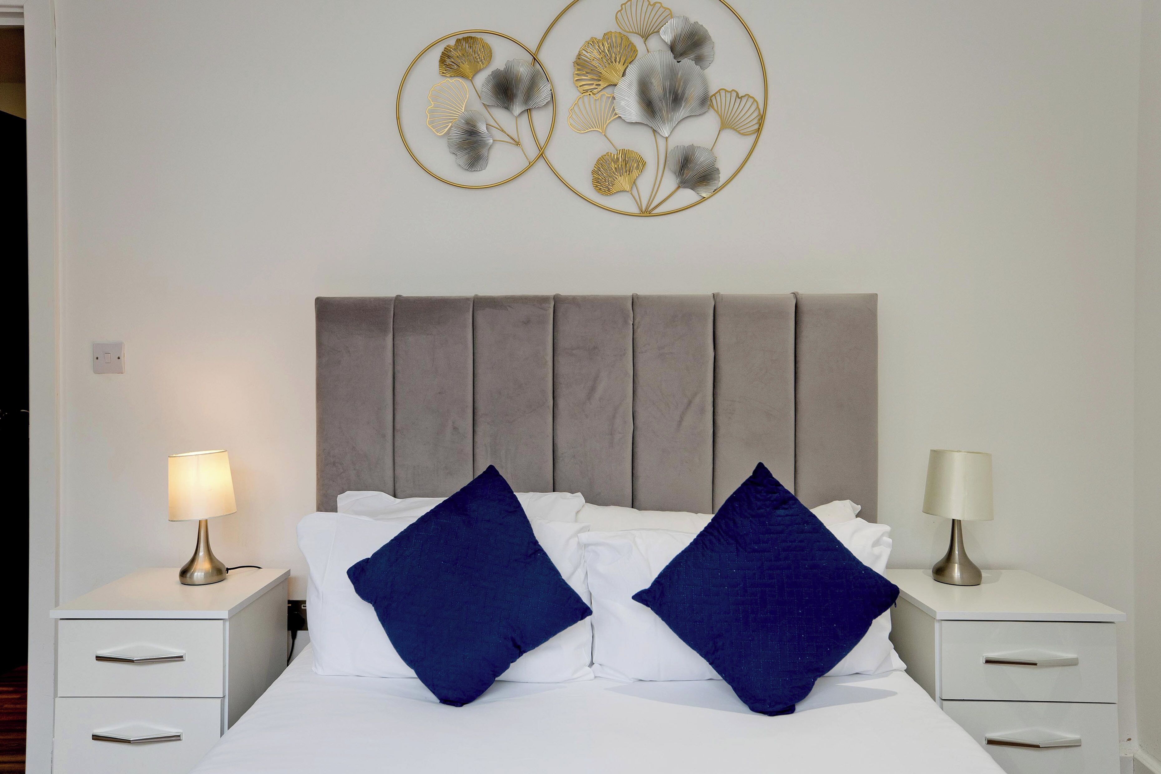 A neatly made bed with two pillows, a bedside table with a lamp, and wall art above the bed.