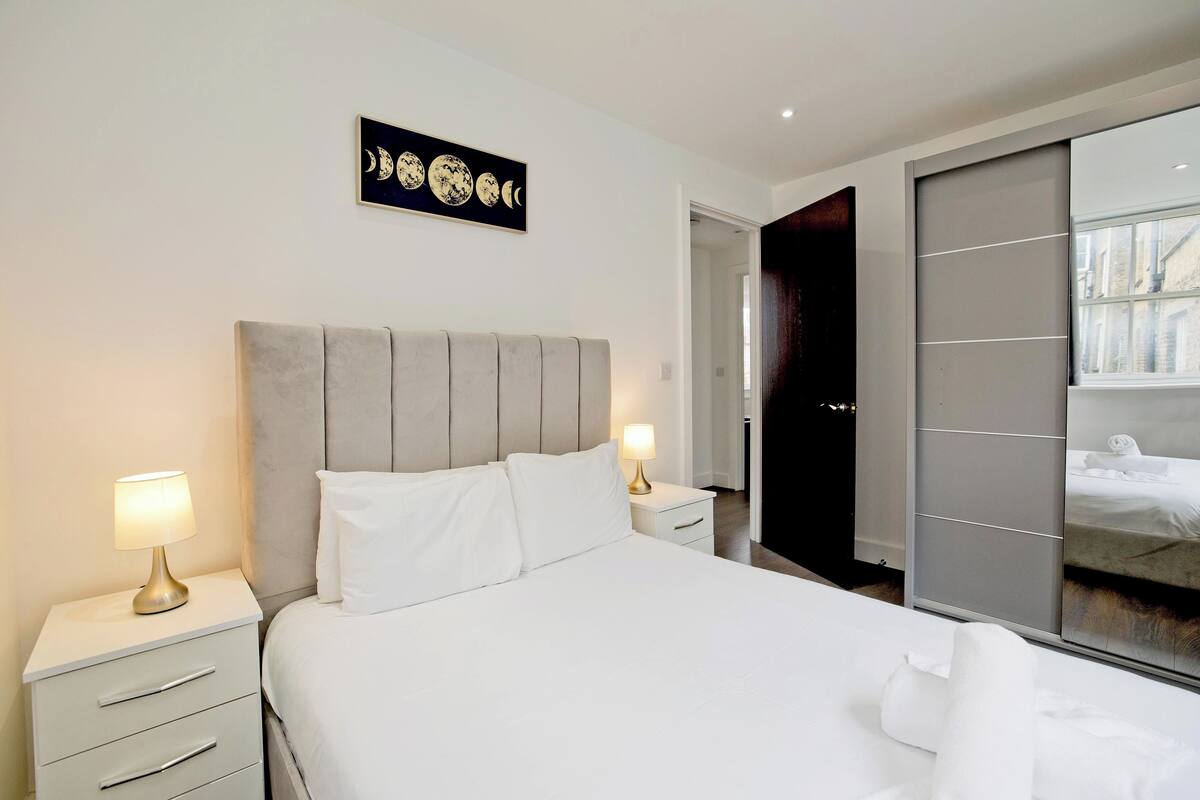 A modern hotel room with a large bed, two bedside tables with lamps, a wall-mounted artwork, and a sliding door closet.