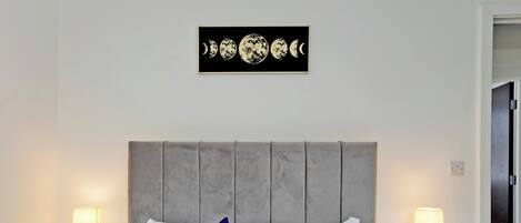 Un lit bien fait, avec deux oreillers bleus, une tête de lit grise et deux tables de chevet avec des lampes.