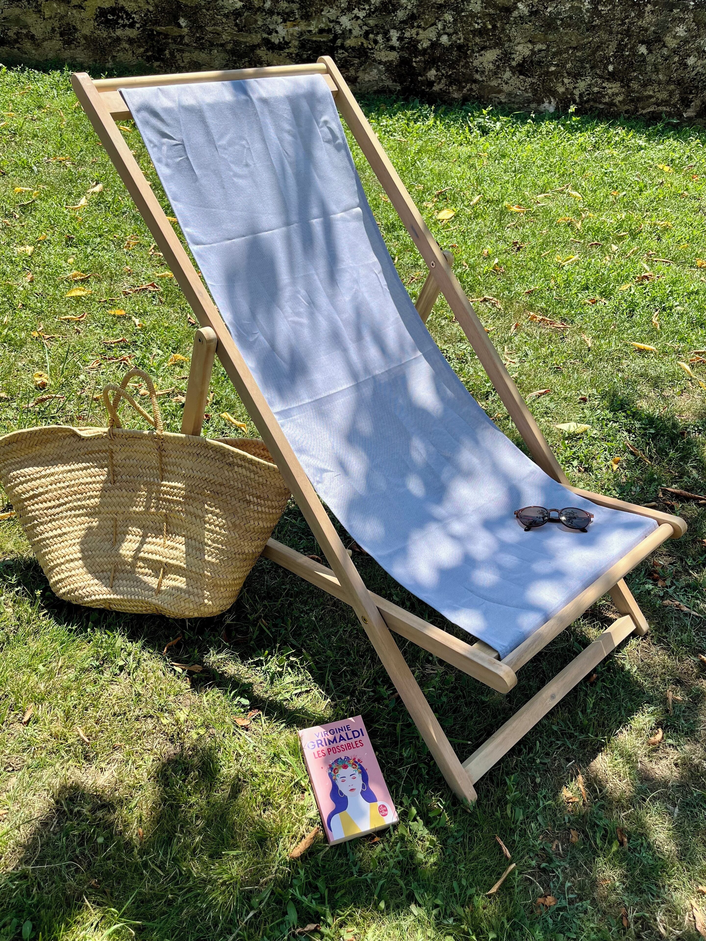 Een houten lounge stoel met een blauw kussen, een gevlochten mand en een boek met de titel 