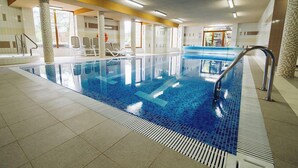 Ein Innenpool mit klarem, blauem Wasser, gefliestem Boden und einigen Liegestühlen.