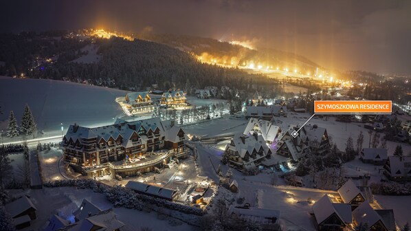 Une station de ski enneigée, dotée de plusieurs chalets, d’un télésiège et d’un bâtiment central illuminé.